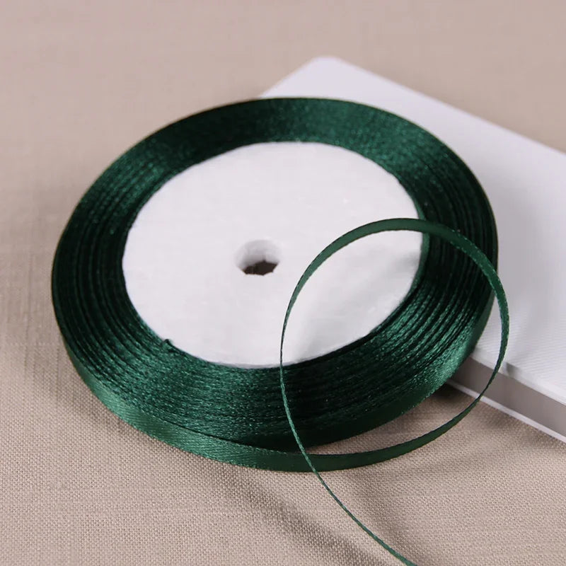 A spool of dark green satin ribbon for gift wrapping and DIY crafts resting on a light surface.