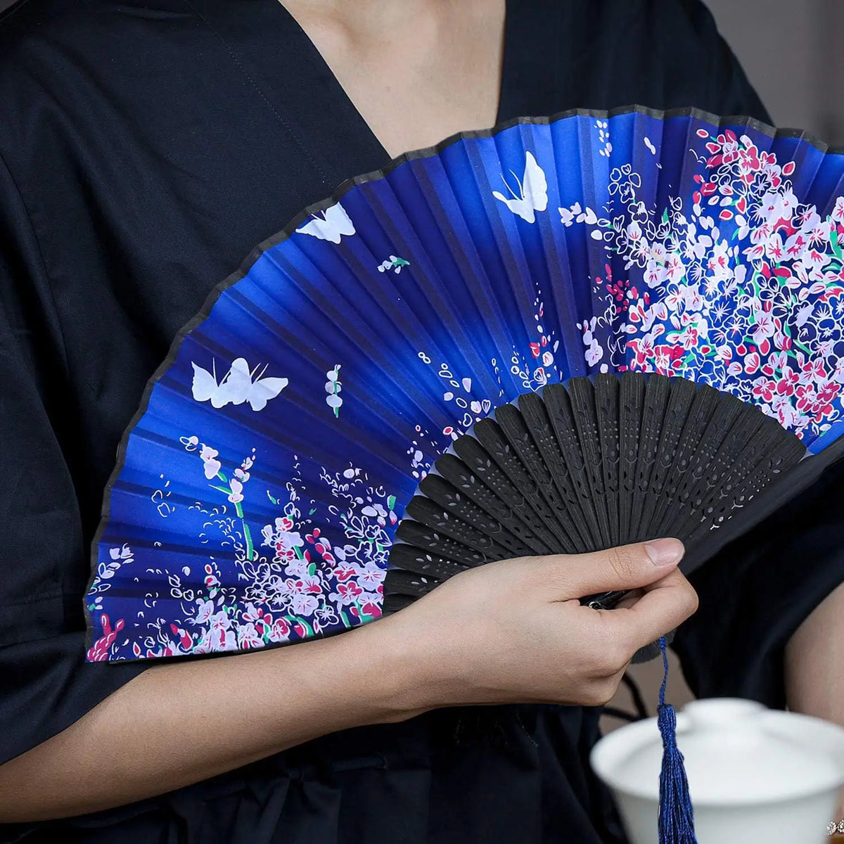 A hand holding a vintage silk bamboo folding fan with blue and pink floral designs.