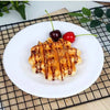 A golden waffle topped with syrup and fresh berries served on a white plate on a black wire rack.