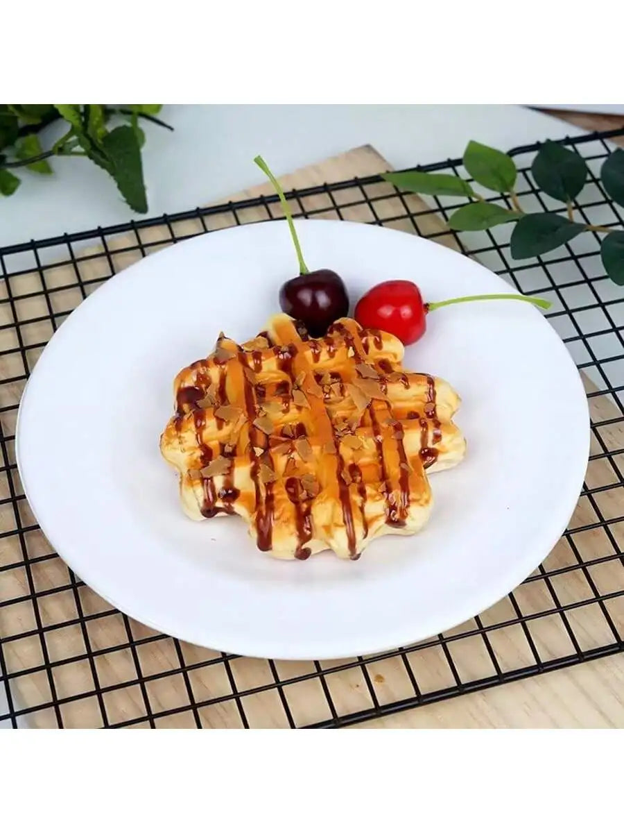 A golden waffle topped with syrup and fresh berries served on a white plate on a black wire rack.
