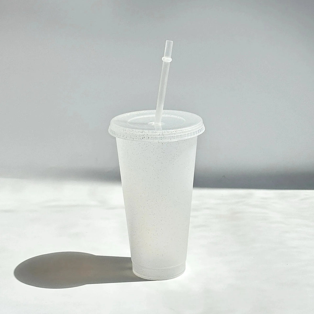 A clear plastic tumbler with a lid and straw is shown against a light gray background.