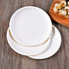 A stack of white, fluted disposable paper plates resting on a wooden board.