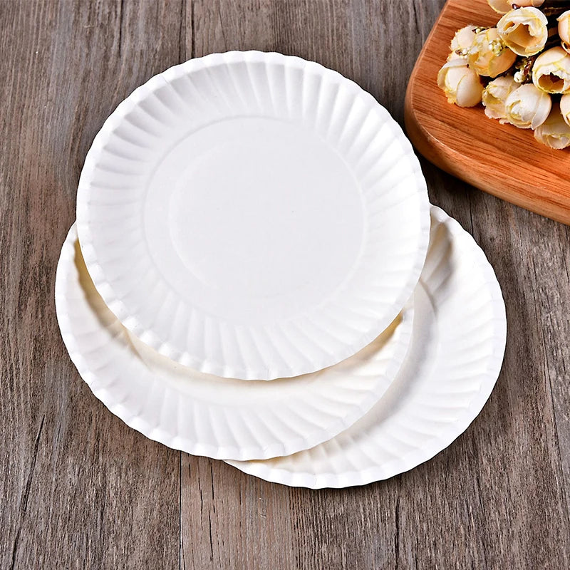 A stack of white, fluted disposable paper plates resting on a wooden board.