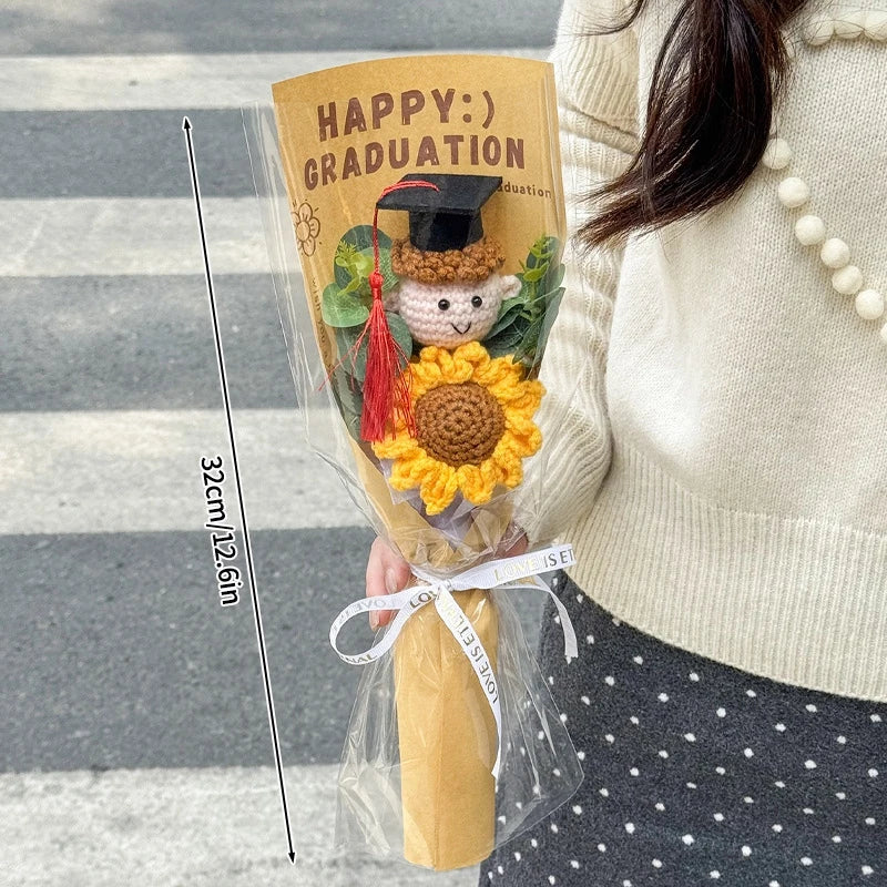 A handcrafted crochet flower bouquet featuring a yellow sunflower and a small teddy bear wearing a graduation cap.