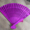 A vibrant purple hand carved bamboo folding fan with intricate cutouts.