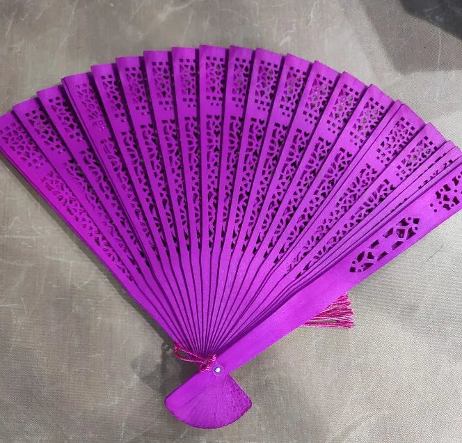 A vibrant purple hand carved bamboo folding fan with intricate cutouts.