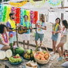 A group of people enjoying a tropical party with colorful Hawaiian leis and fruit on a beach.