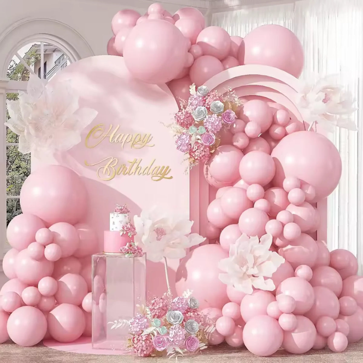 A large arrangement of pastel pink latex balloons and floral accents for a birthday party display.