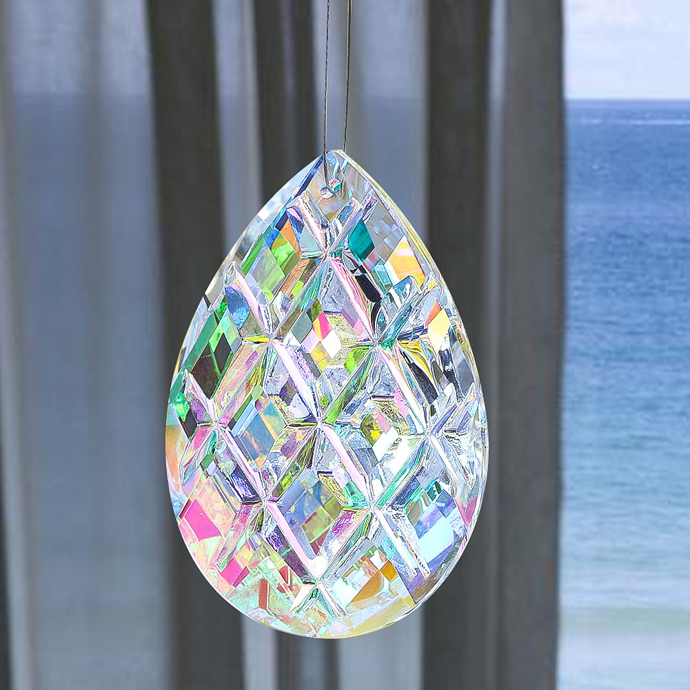 A teardrop-shaped crystal prism sun catcher hanging in front of a window with a view of the ocean.