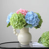 A vase holds a bouquet of artificial hydrangea stems in shades of pink, blue, and green.