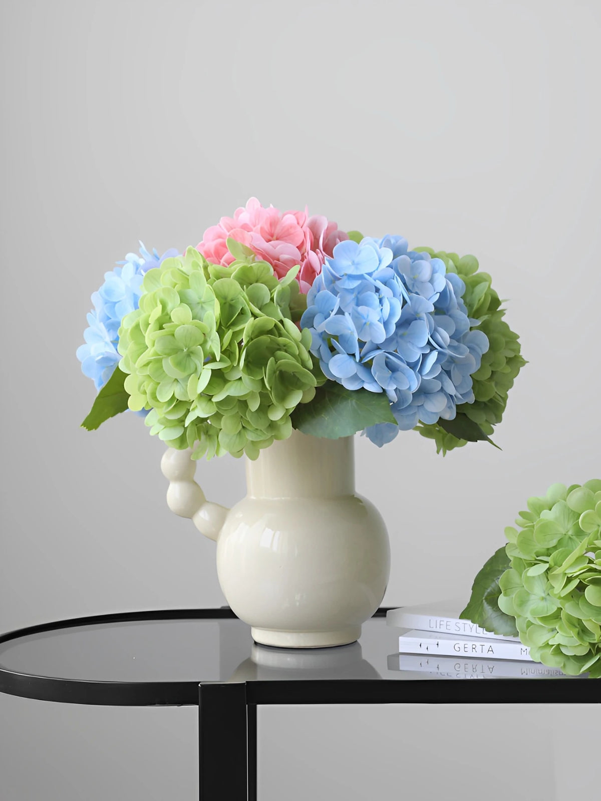 A vase holds a bouquet of artificial hydrangea stems in shades of pink, blue, and green.