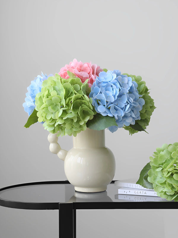 A vase holds a bouquet of artificial hydrangea stems in shades of pink, blue, and green.