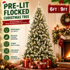 A fully decorated pre-lit flocked Christmas tree with warm white LED lights standing in a festive indoor setting.