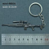 A silver miniature assault rifle model is displayed next to a metal keyring and a ruler for scale.