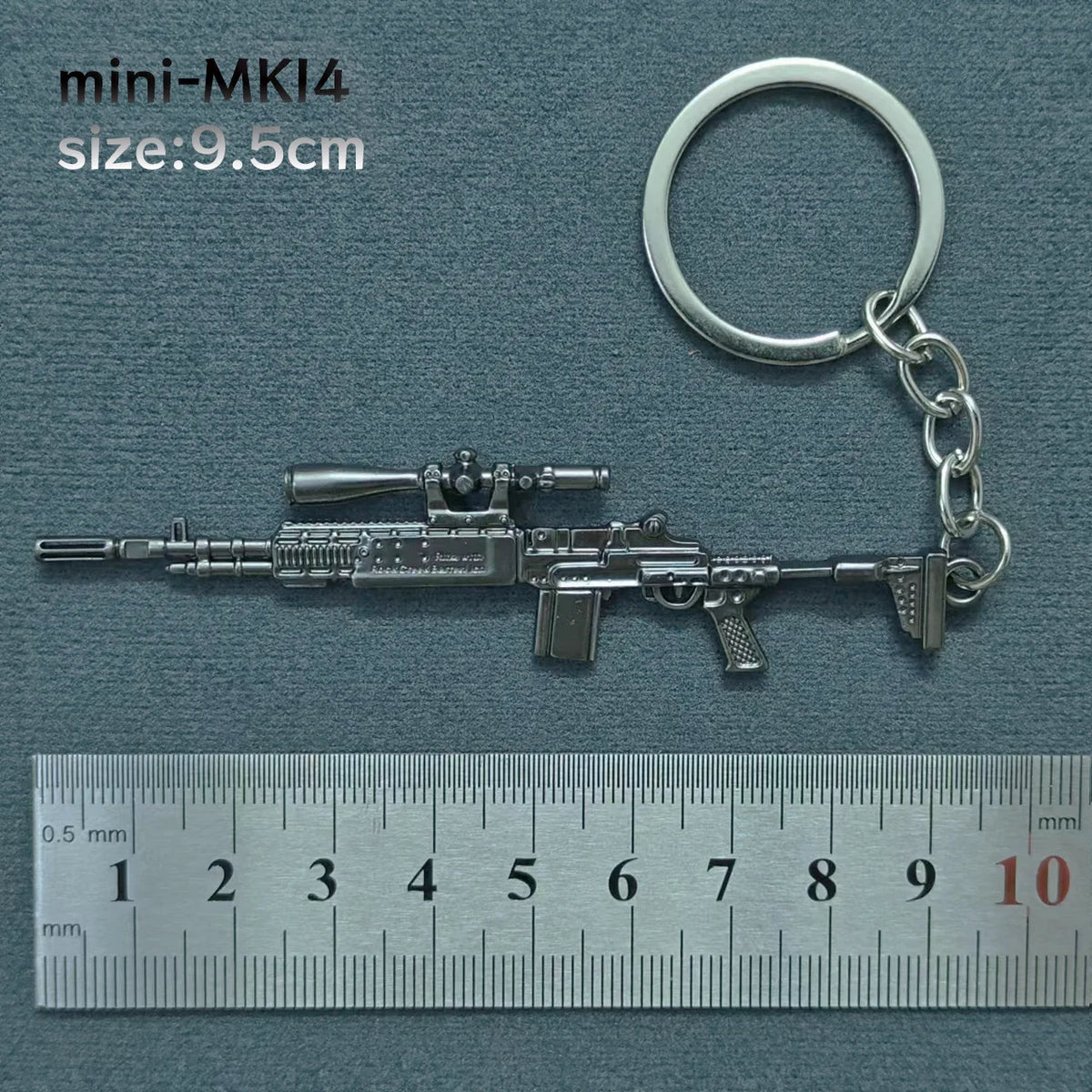 A silver miniature assault rifle model is displayed next to a metal keyring and a ruler for scale.