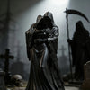 A dark collectible figurine of a hooded figure embracing another, set in a gothic decor scene.