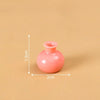A small, round, pink resin vase with a narrow opening is shown against a neutral background.