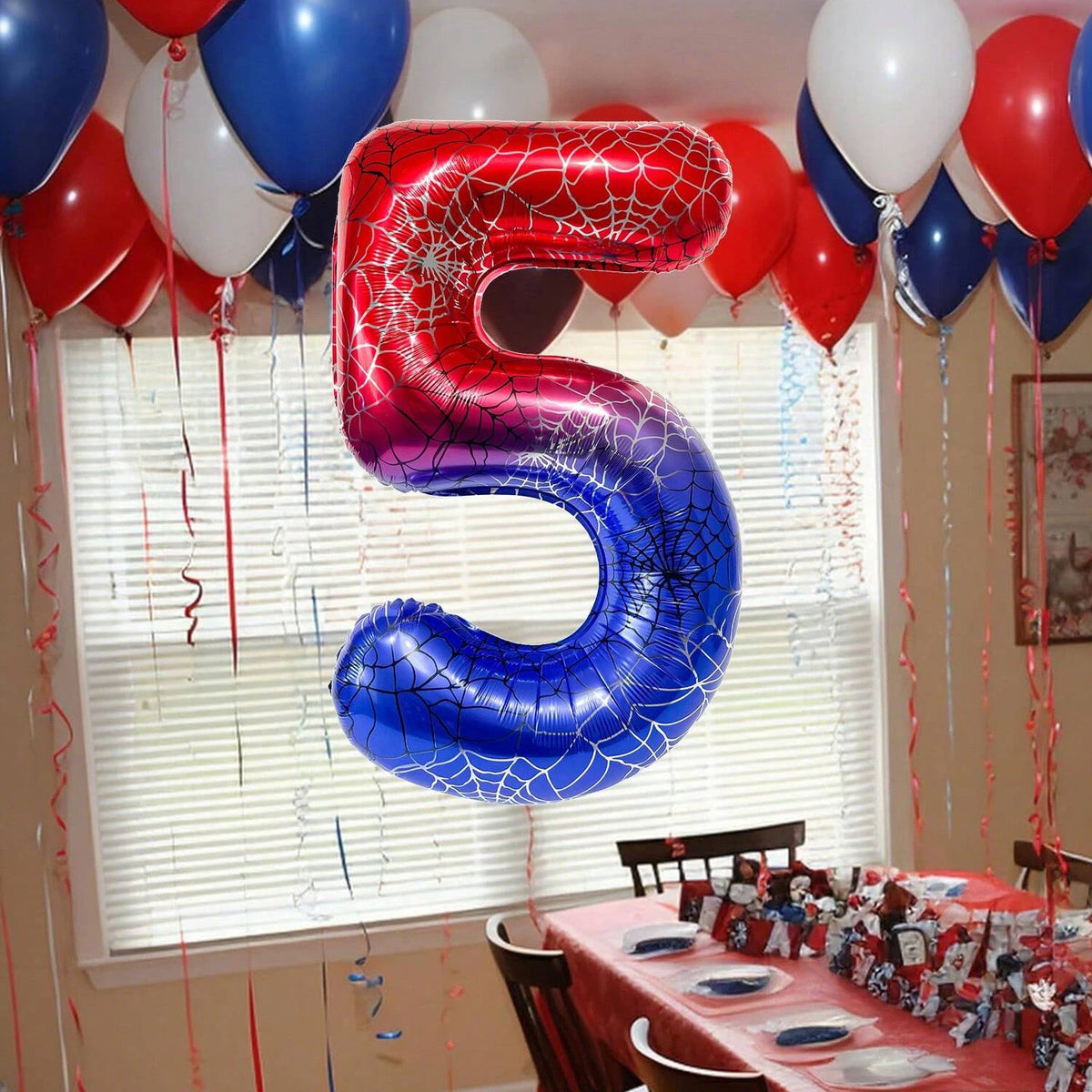 A large red and blue spiderweb number foil balloon shaped like the number 5 is displayed in front of a window.