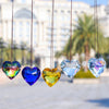 Five hanging glass heart pendants in various rainbow colors suspended against a blurred outdoor background.