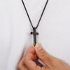 A black stainless steel cross pendant necklace with the inscription I'm strong and courageous is being held by a hand against