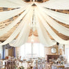 Elegant white sheer chiffon drapery suspended from a chandelier in a rustic wooden venue for a wedding event.