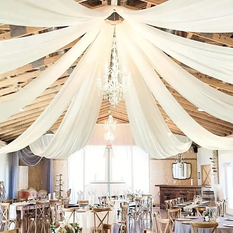 Elegant white sheer chiffon drapery suspended from a chandelier in a rustic wooden venue for a wedding event.