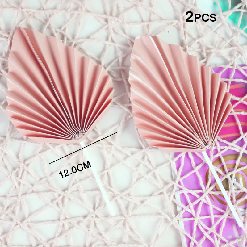 Two pink palm leaf cake toppers with pleated texture displayed on a white surface.
