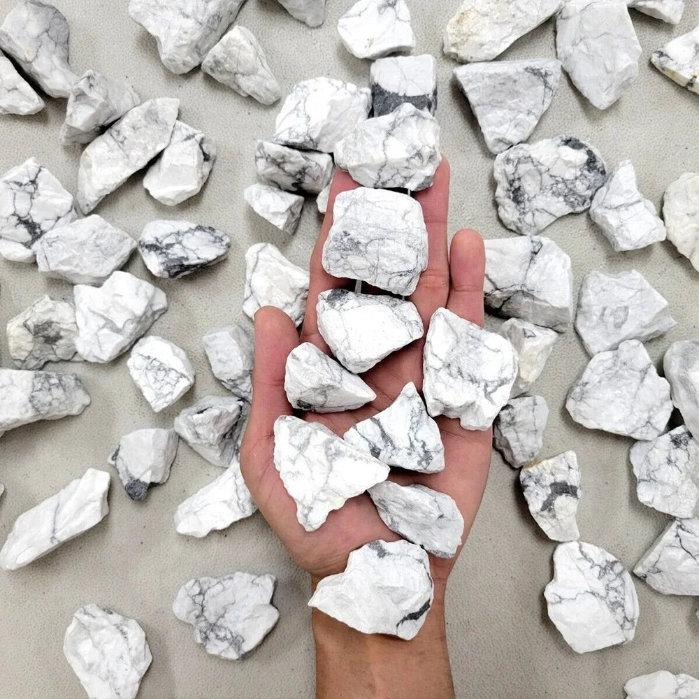 A hand holds a collection of white and gray natural raw healing crystal stones for chakra balancing and home decor.