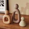 A set of three modern resin family statues in beige and brown tones displayed on a wooden surface.