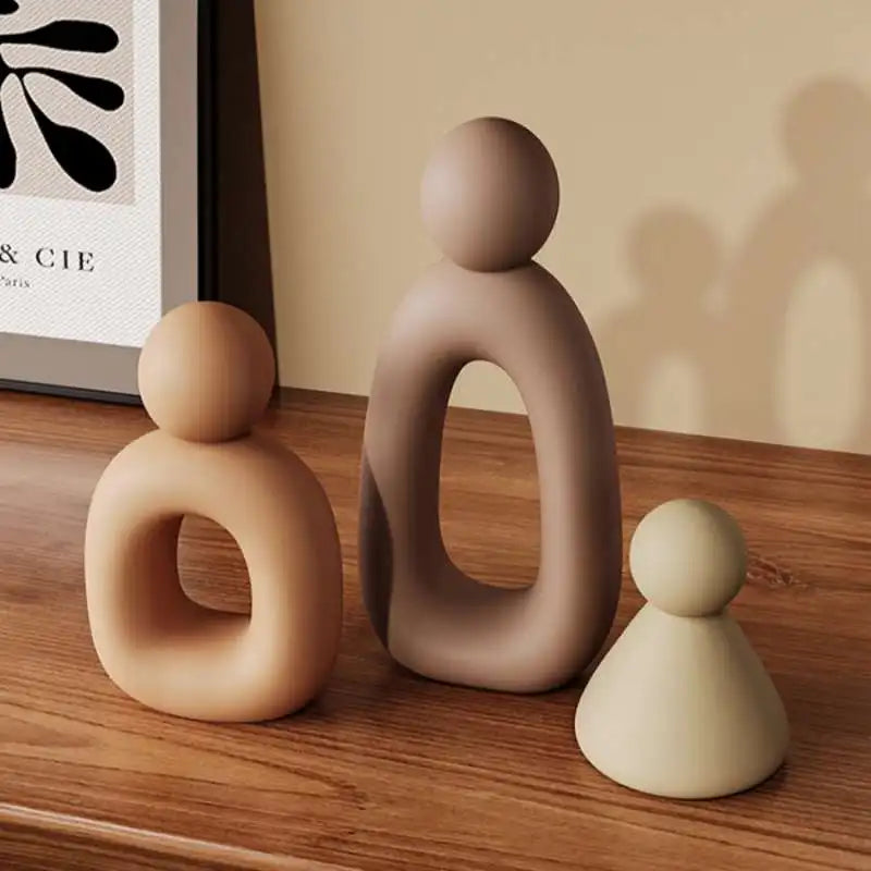 A set of three modern resin family statues in beige and brown tones displayed on a wooden surface.