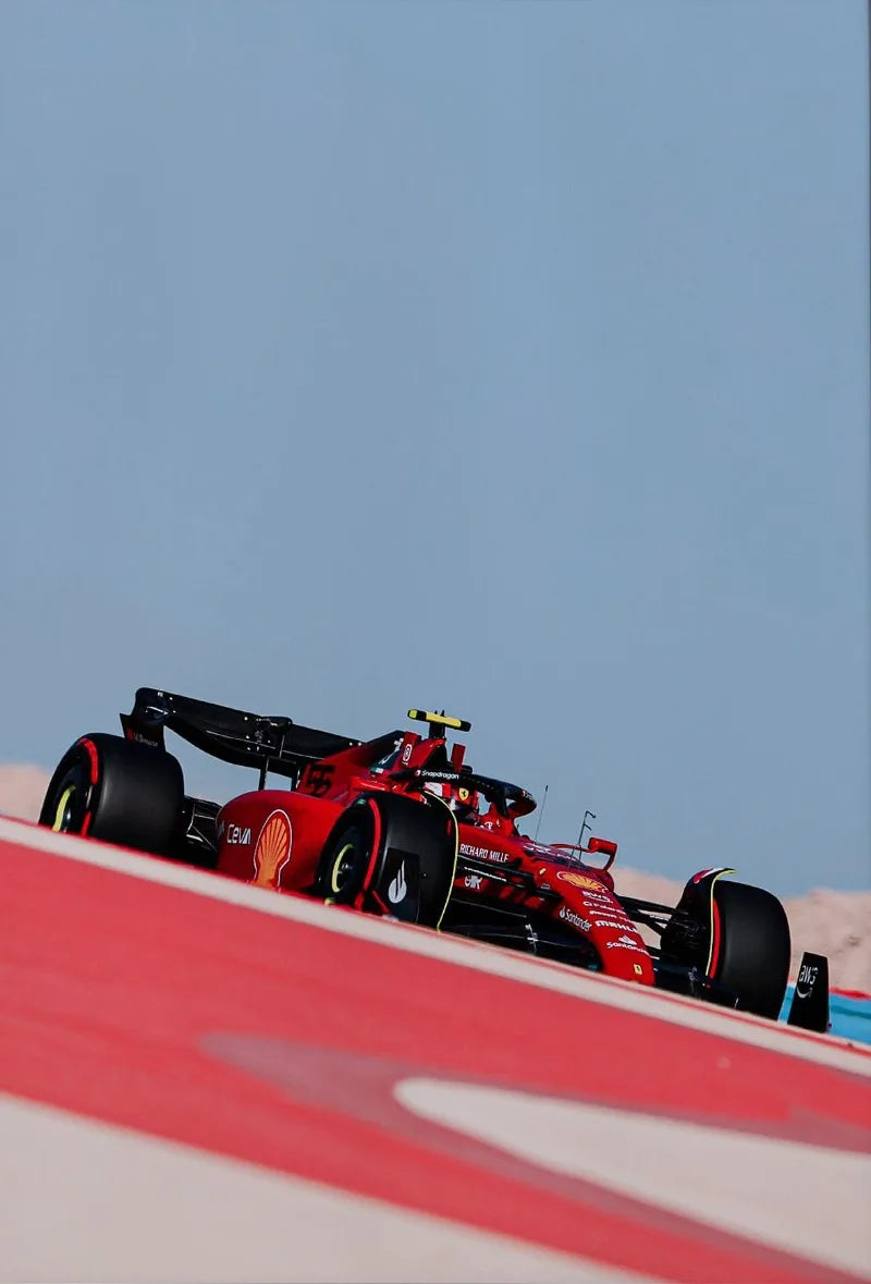 A red Formula 1 car is shown in profile on a track wall, set against a clear blue sky.