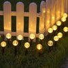 A row of white picket fence posts illuminates a lawn with glowing solar powered bubble ball garden lights.