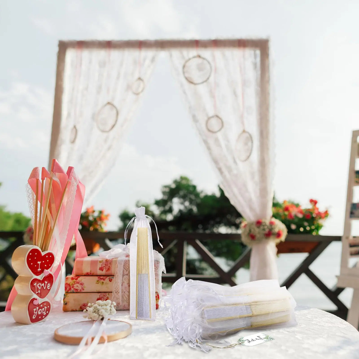 Elegant paper hand fans displayed with gift bags and thank you cards on a white table.
