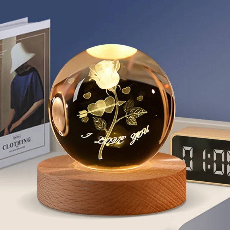 A round amber crystal ball decoration with a gold rose and the text I love you engraved inside, resting on a wooden base.
