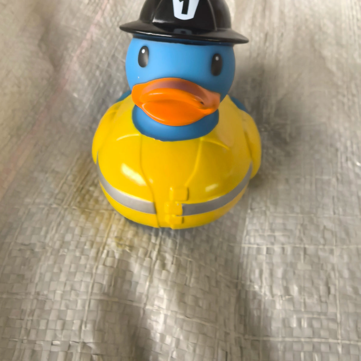 A yellow rubber duck toy with a blue head and black hat sitting on a silver-colored surface.