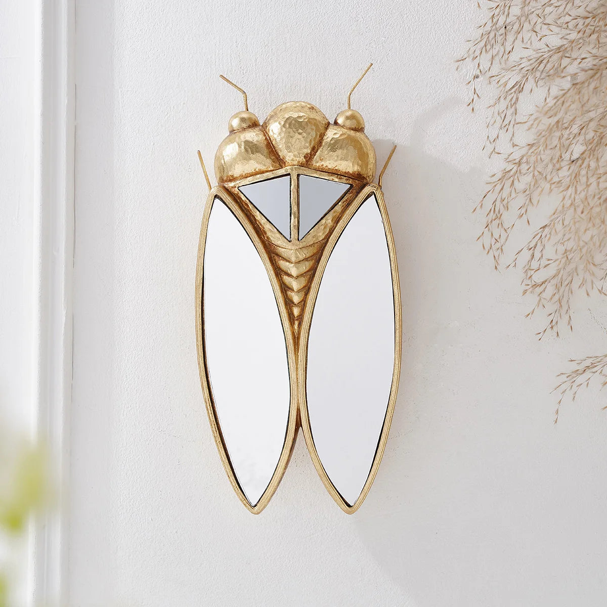 A golden cicada hanging ornament made of resin with iridescent wings mounted on a white wall.