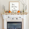 A white fireplace mantel decorated with an artificial maple leaf garland, pumpkins, and a framed sign that reads Stay Spooky 