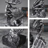 A set of three resin figurines depicting hands and faces, rendered in a textured, monochromatic style.