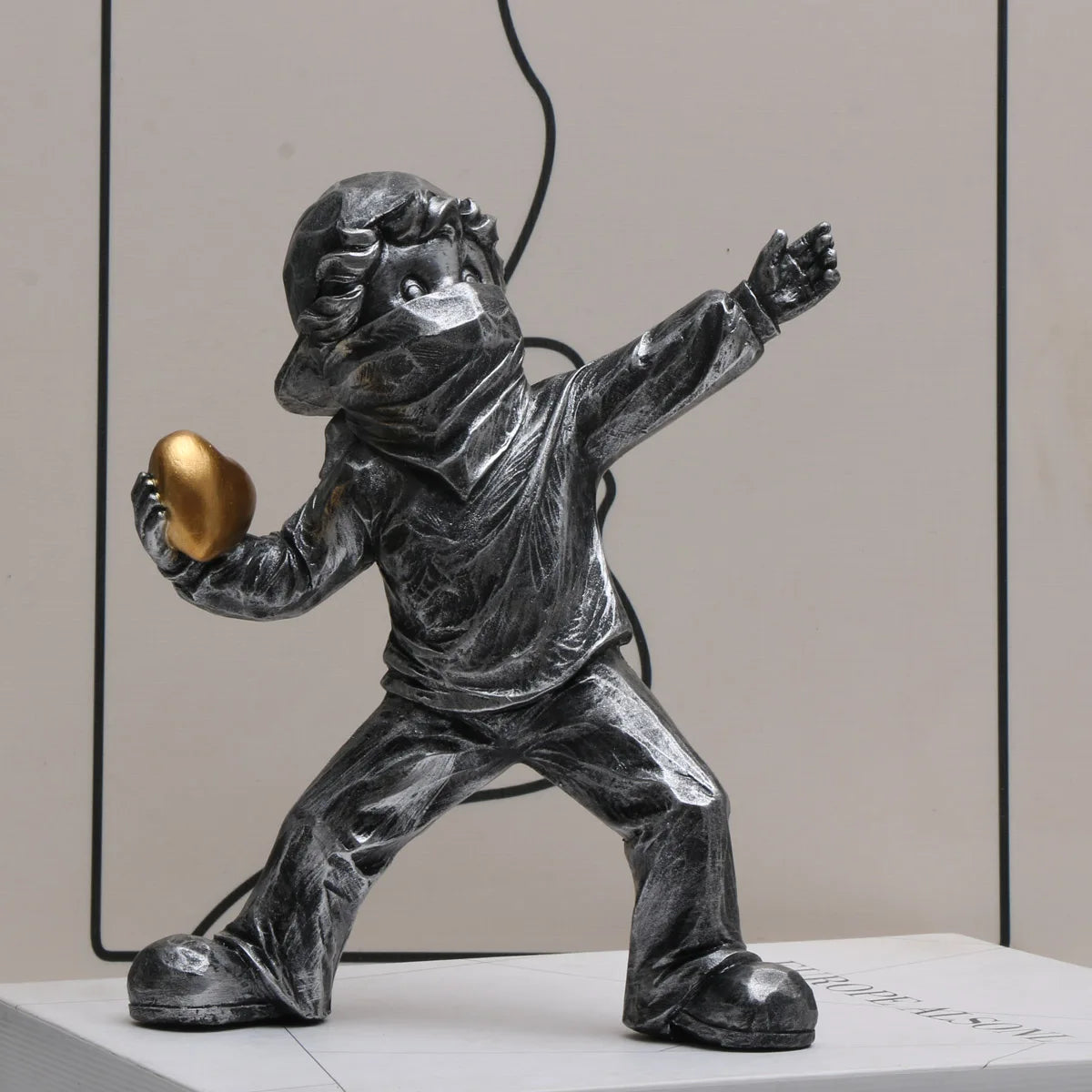 A dark resin sculpture of a child figure throwing a golden object.