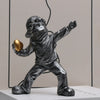 A dark resin sculpture of a child figure throwing a golden object.