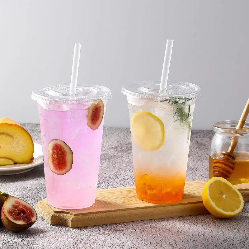 Two clear plastic cups filled with colorful iced beverages, garnished with citrus slices and mint, resting on a wooden board.