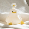 A white ceramic duck night light with a yellow flower on its head resting on a white fabric.