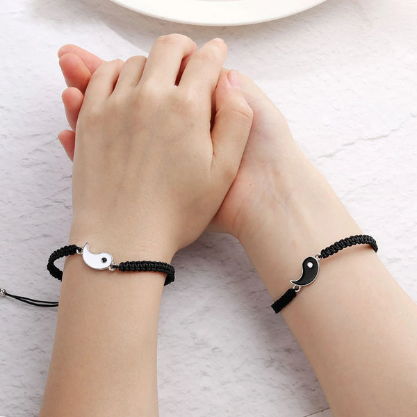 A pair of hands holding a black braided bracelet set with silver charms on a person's wrist.