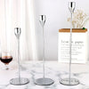 A set of three silver metal taper candle holders displayed on a white marble surface.