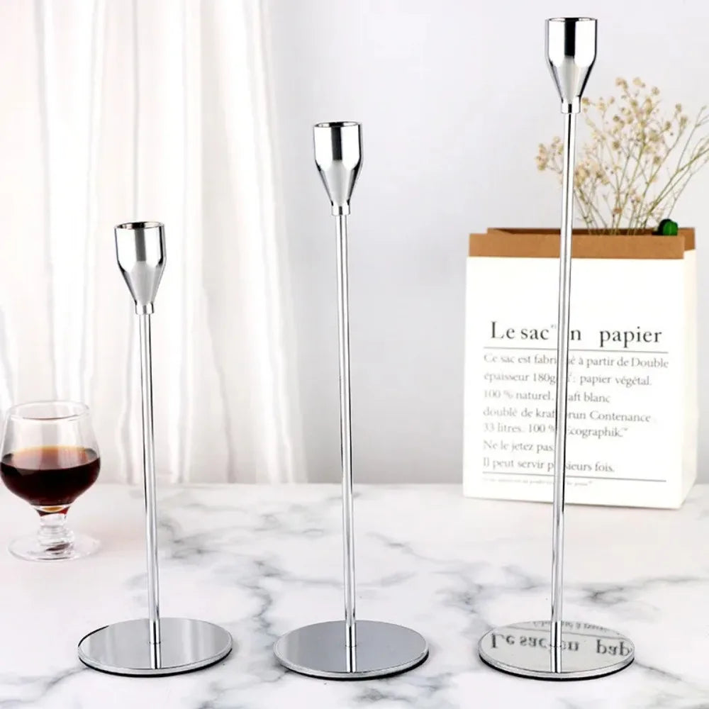 A set of three silver metal taper candle holders displayed on a white marble surface.