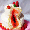 A white layer cake with a section cut open revealing bright red fruit and gold leaf decorations.
