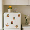 A white refrigerator decorated with several photo frame magnets featuring wooden frog hair styles.