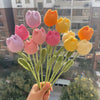 A bouquet of handmade crochet tulips in shades of pink and orange, displayed against an outdoor background.