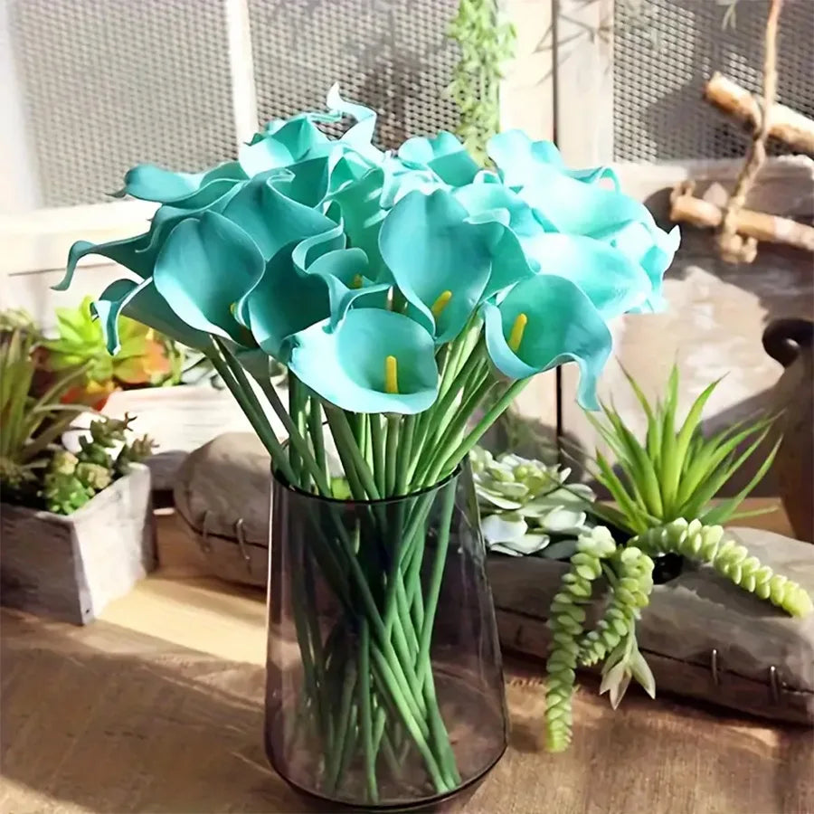 A bouquet of five light blue calla lily stems in a glass vase on a wooden surface.