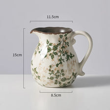 A rustic ceramic milk pitcher with a cracked glaze and pastoral floral design, shown against a light gray background.